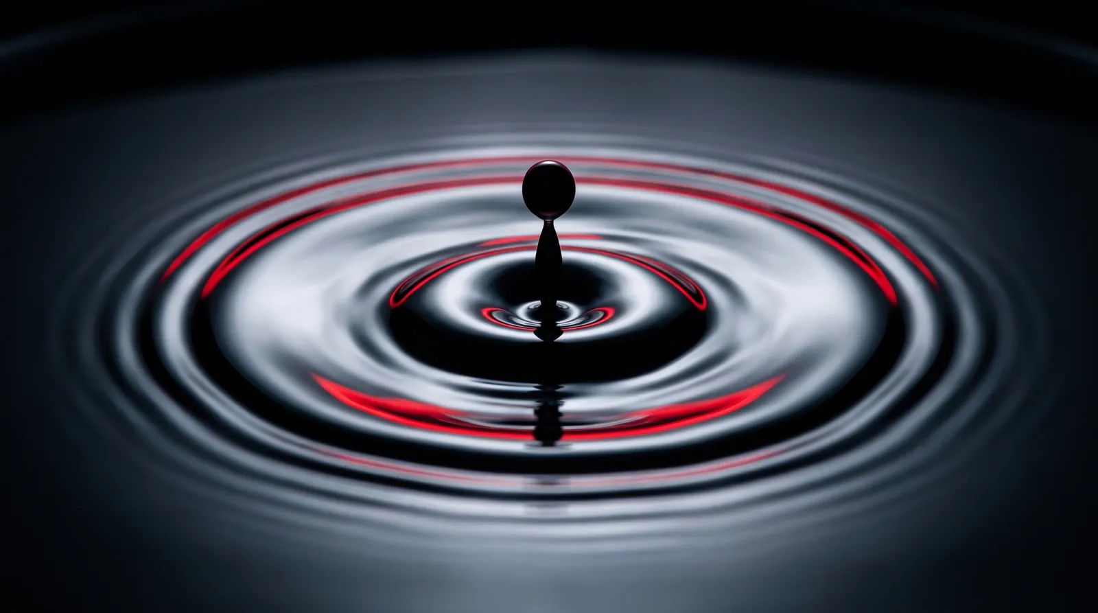Ein Tintentropfen fällt in dunkles Wasser und zieht rote Ringe