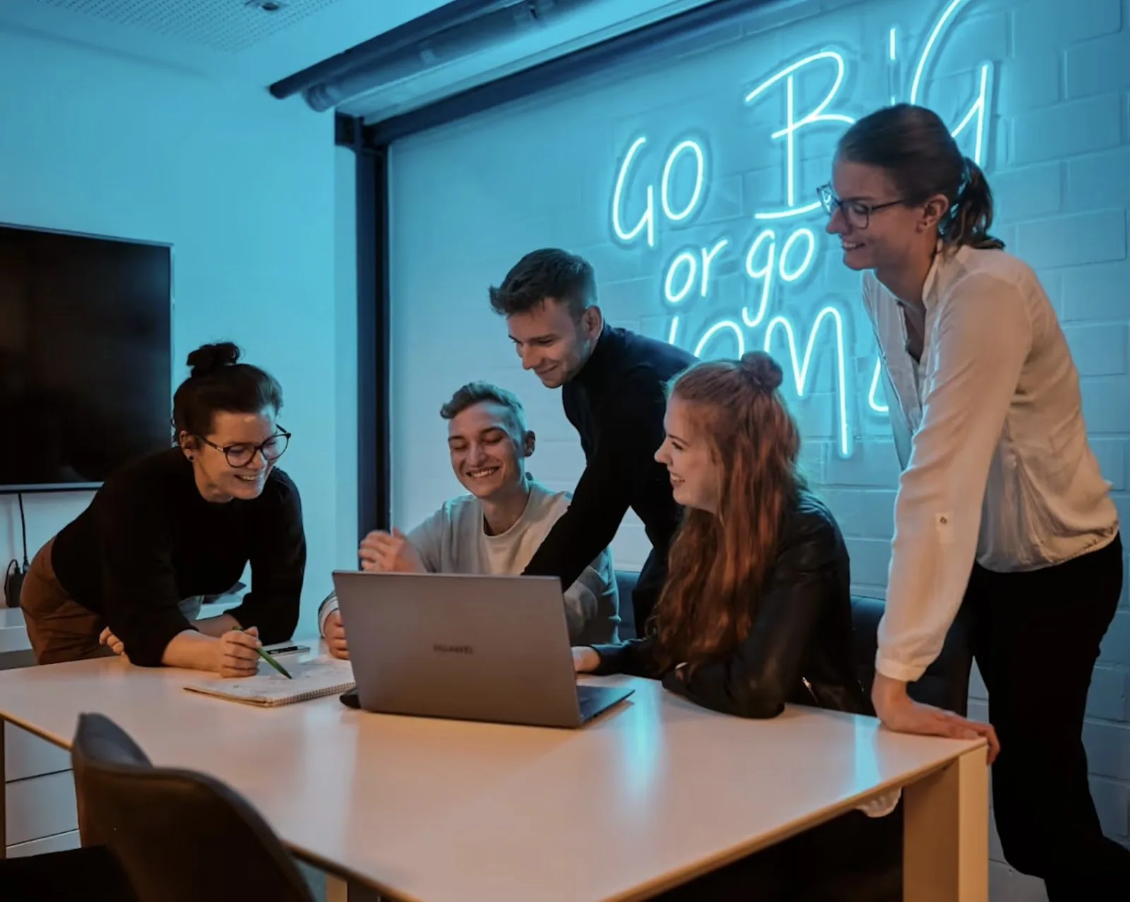 Suchhelden-Team bespricht eine SEO-Strategie am Laptop vor dem Neonschriftzug „Go big or go home“